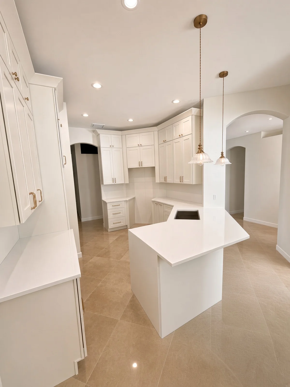 White kitchen with glass pendants over a quartz island and arched doorways