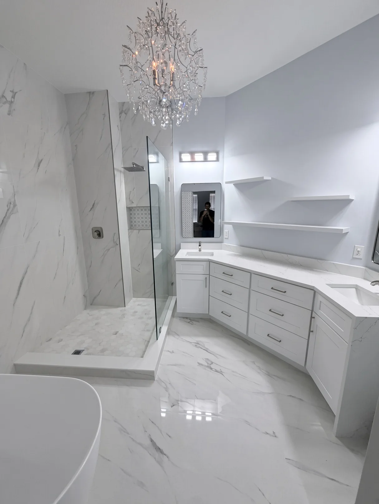White bathroom with a crystal chandelier, glass shower and marble-look tile