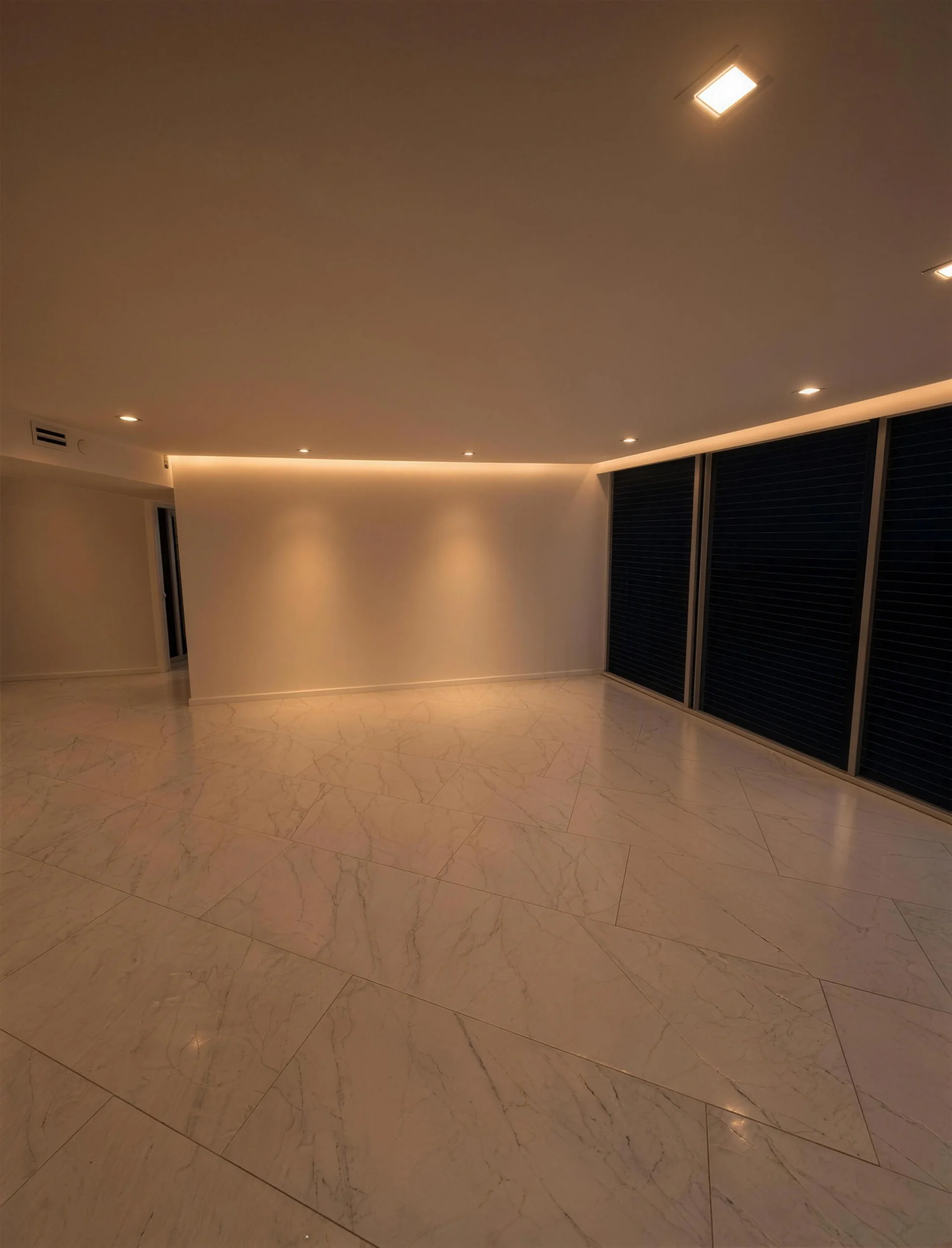 Open living room with warm cove lighting and large marble-look floor tile