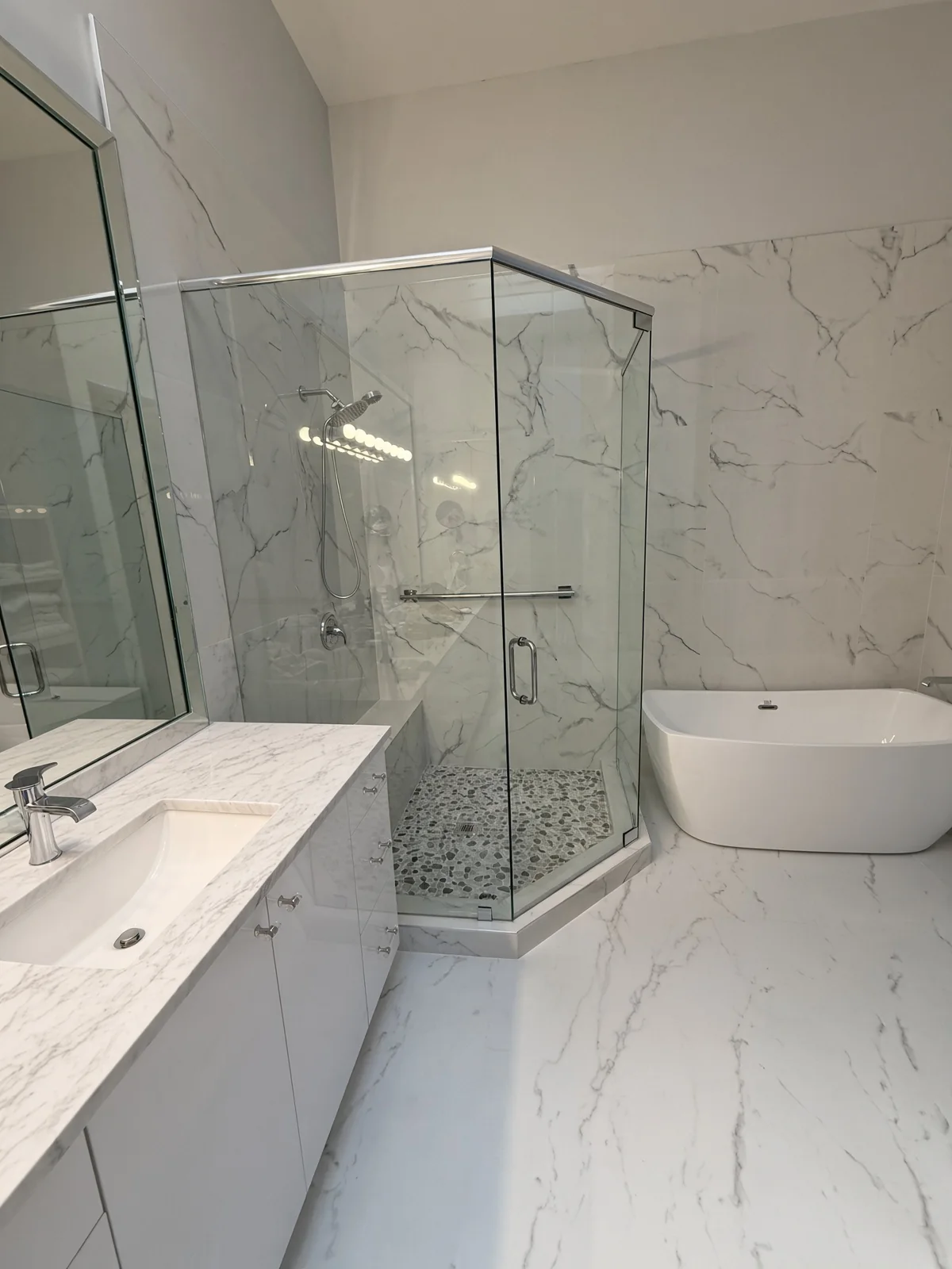 Frameless glass shower with marble-look tile beside a freestanding tub