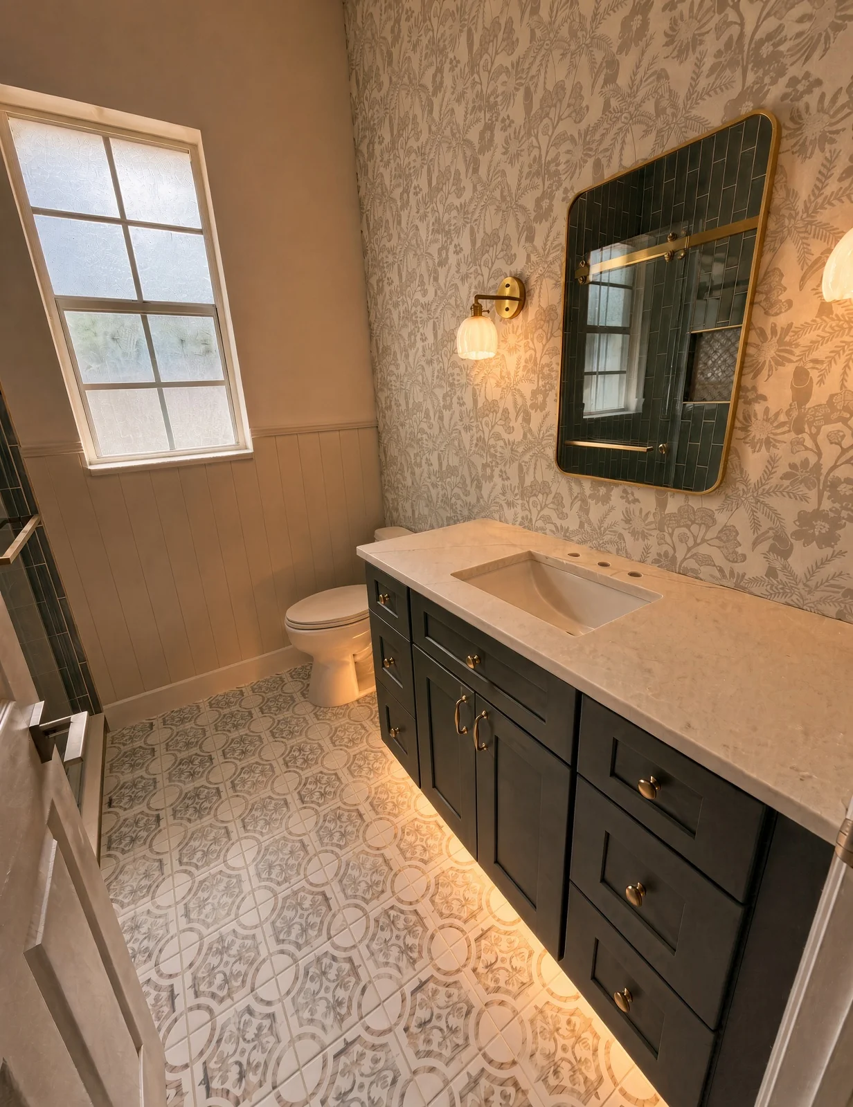Powder room with a navy vanity lit from below, a brass mirror and botanical wallpaper