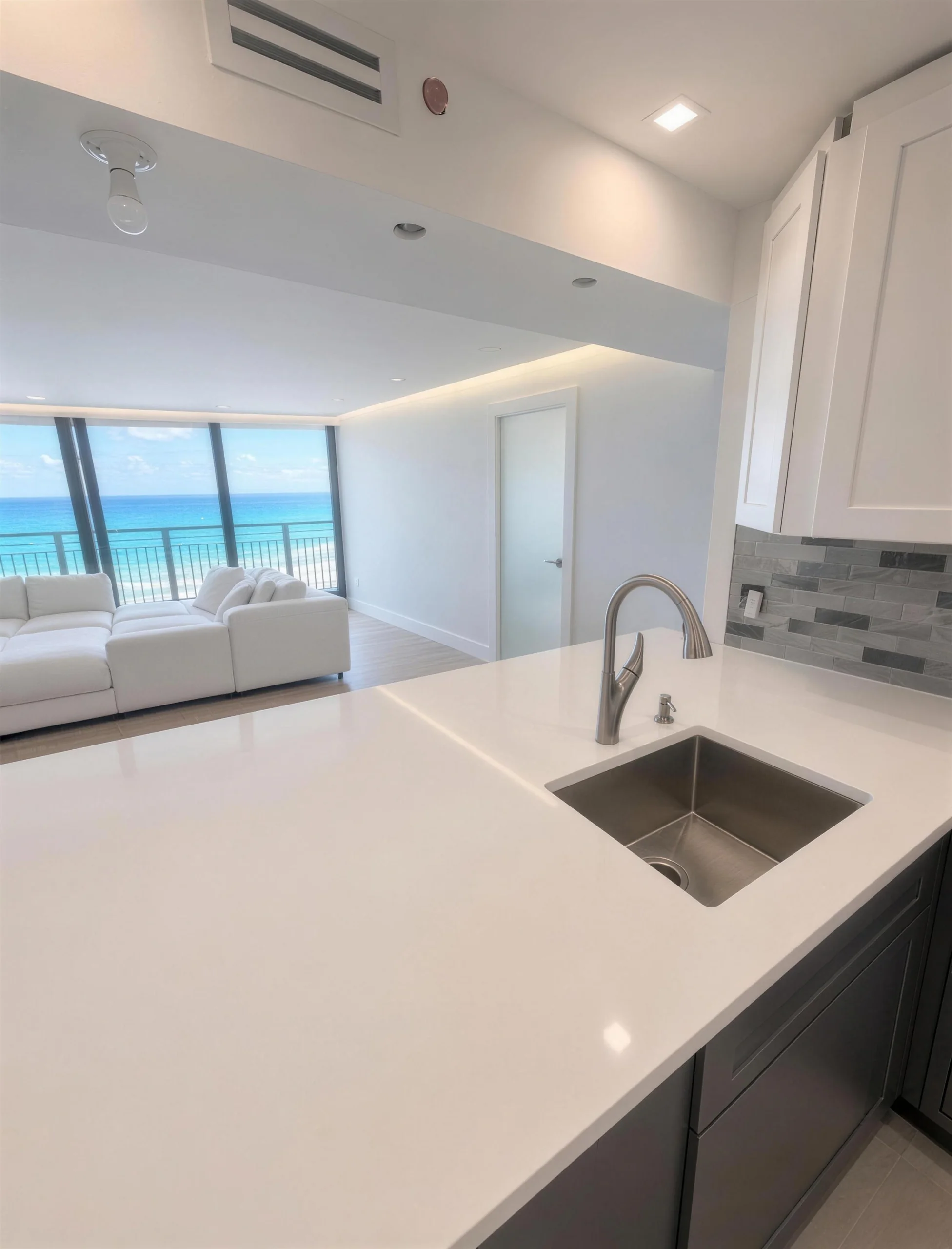 White quartz kitchen counter and sink looking across a living room to the ocean