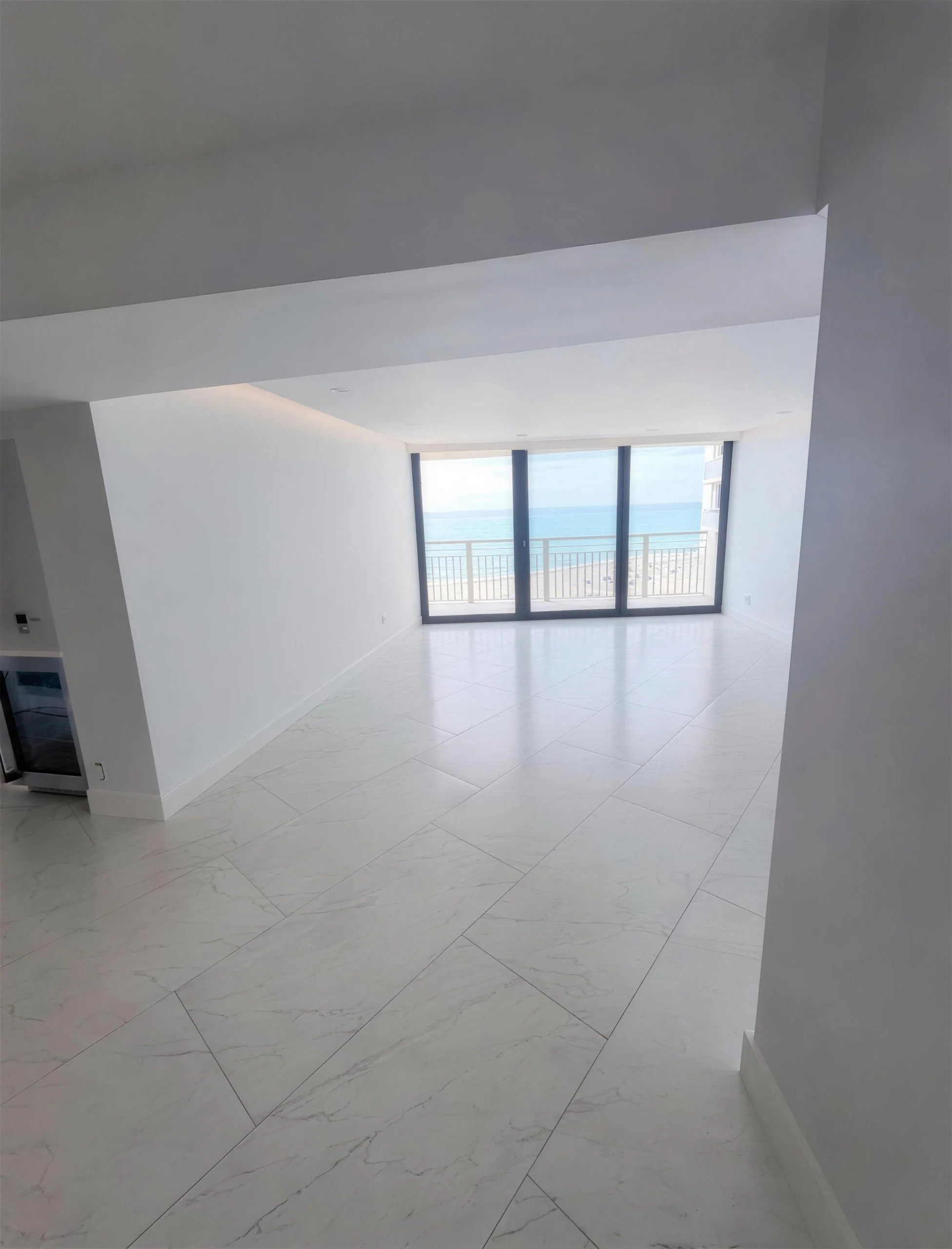 Bright living space with marble-look tile leading to ocean-view windows