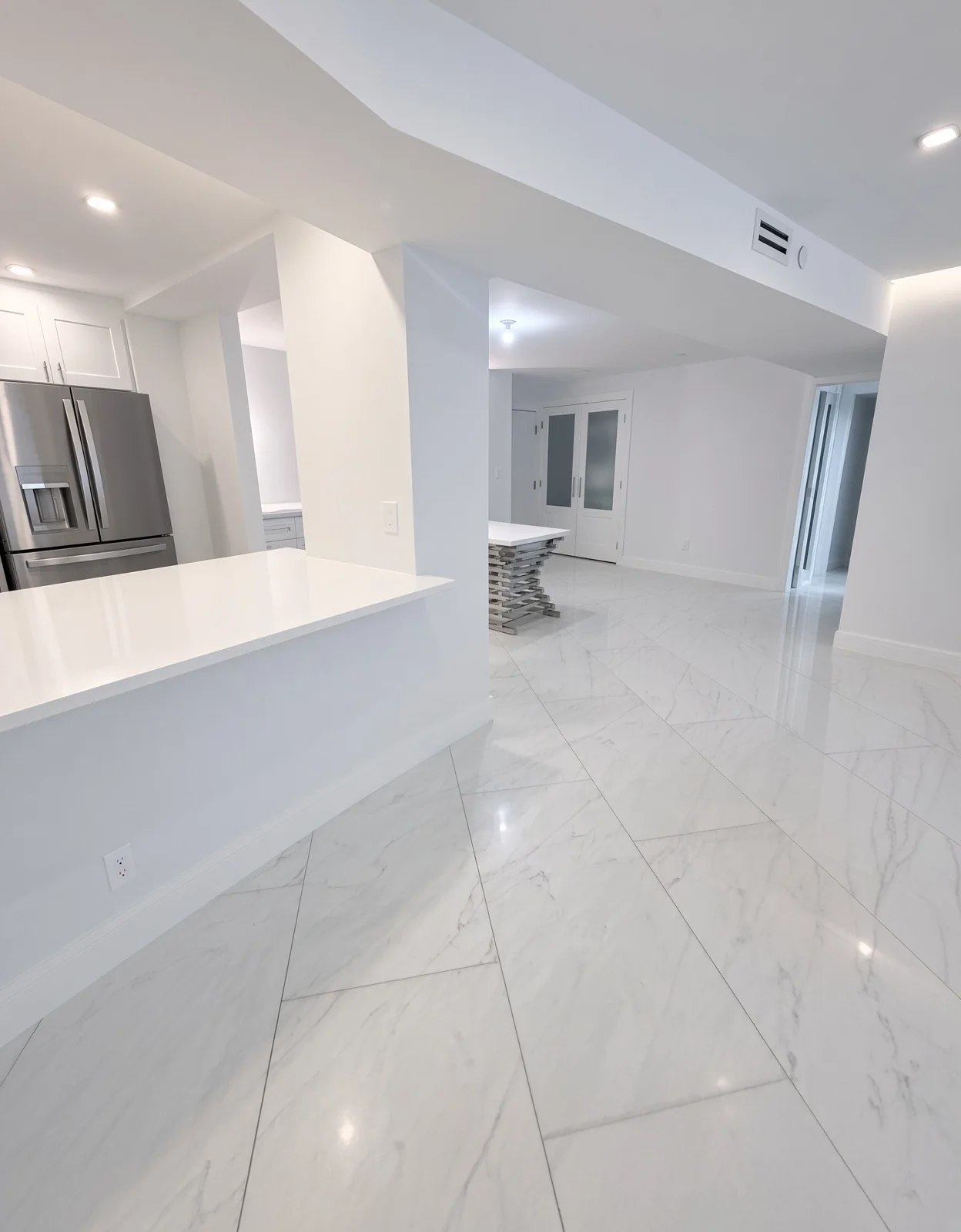 Open-plan unit with a white kitchen peninsula and glossy marble-look tile