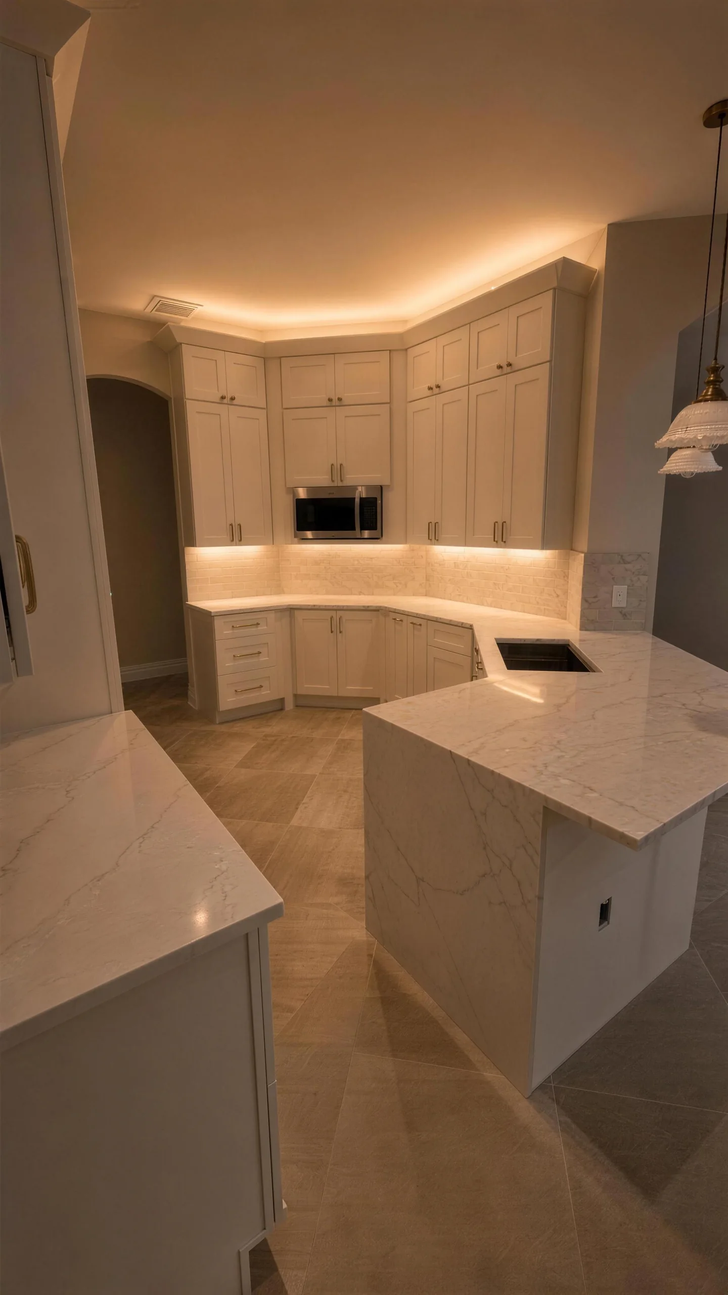 Kitchen at night with glowing crown and under-cabinet lighting, white cabinetry and a marble-look island